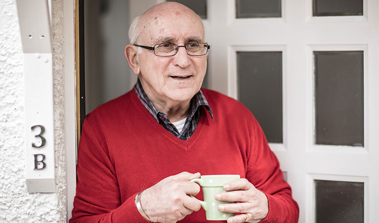 Old man with cup of tea at front door