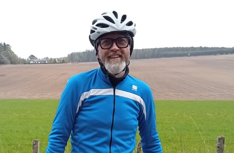 John Todd, heart attack survivor, stands in cycling gear against a countryside background