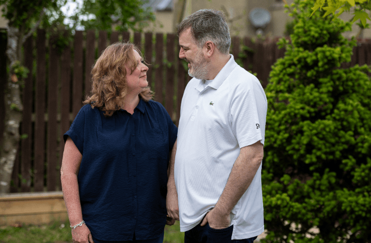 Husband and wife stand looking at each other in a garden