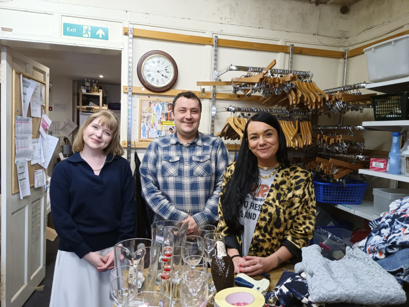 Two volunteers stand in the charity shop stockroom with the store manager.